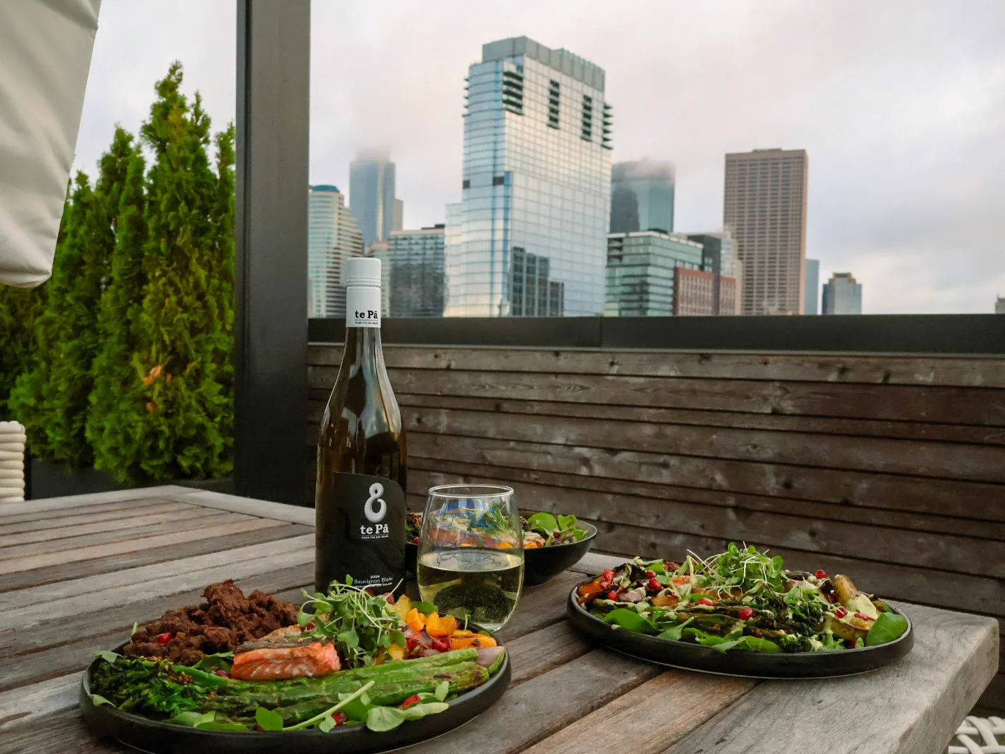 Minneapolis rooftop dinner: dark plates of grass-fed brisket, wild salmon, charred greens against the downtown skyline.