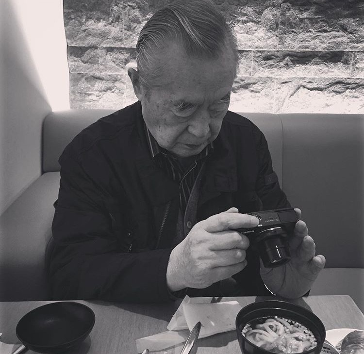 Dr. Yoshiro Nakamatsu photographing his meal at a restaurant table, a practice he has sustained for fifty-five years.
